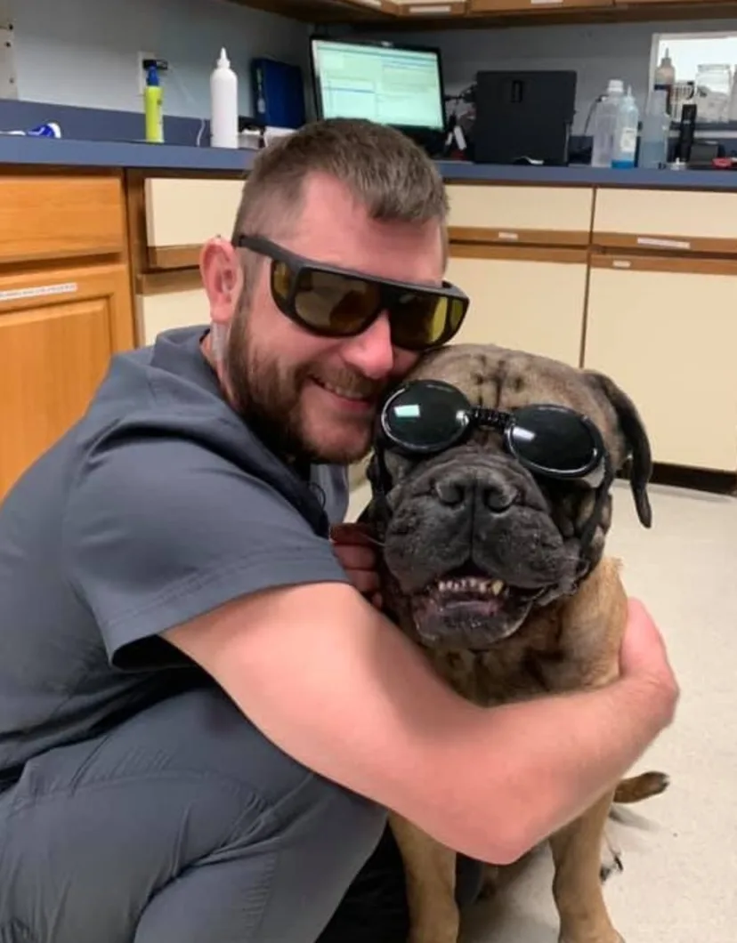 Tony wearing protective glasses and hugging dog also wearing protective glasses at Strawbridge Animal Care